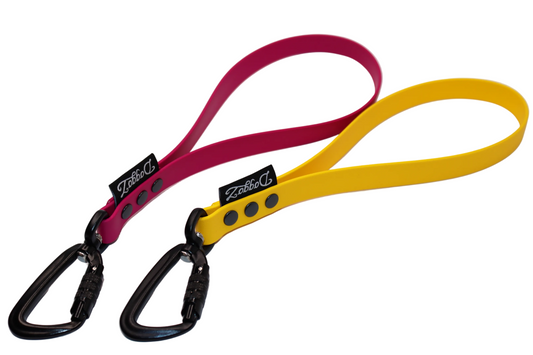 Two BioThane traffic handles in Pink Magenta and Yellow Sunflower, each featuring a black aluminum locking carabiner, matching black rivets, and the DoggoZ brand label.